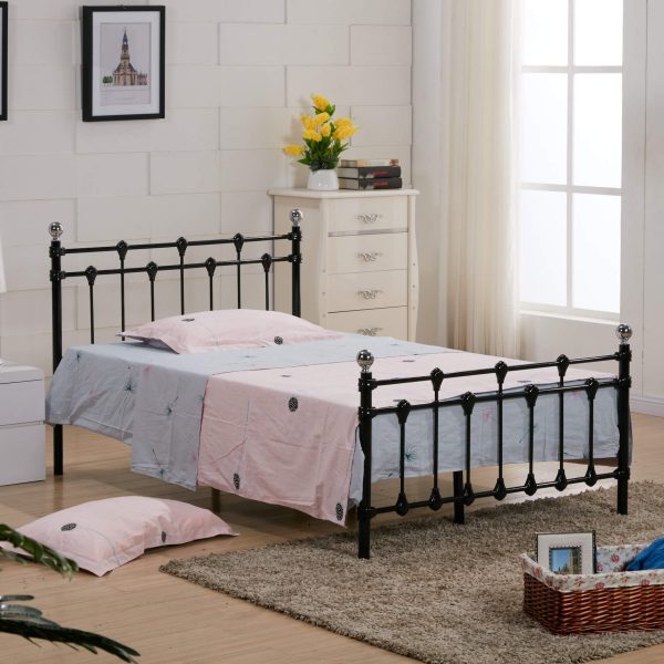 Rochelle Double Bed in black metal frame with polished chrome caps, light-colored bedding, white dresser, yellow flowers, and a wicker basket in a well-lit bedroom.